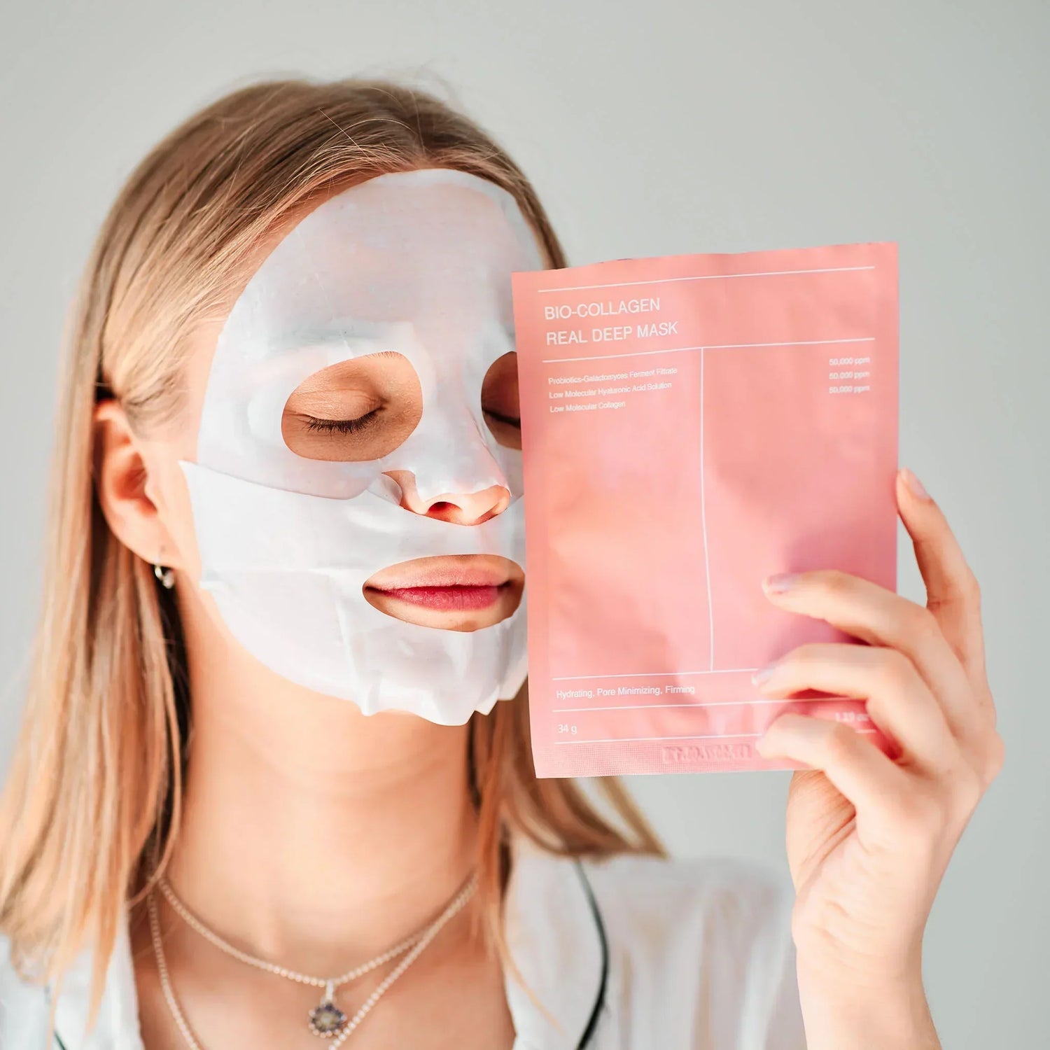 Woman with glowing skin wearing a bio-collagen face mask while holding the product packaging – deep hydration and anti-aging skincare